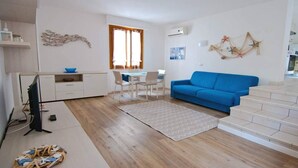 A modern living room with a blue sofa, a dining area with a table and chairs, and a kitchen area with a white cabinet. - Just 300 meters from the sandy beach (Marina di Campo)