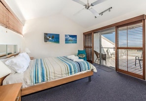 Ein Schlafzimmer mit einem Bett, einem Deckenventilator, einem Fenster mit Jalousien und zwei Wandbildern.