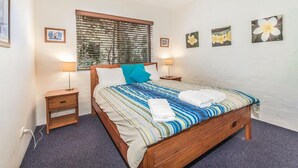 Ein Schlafzimmer mit Bett, einem Fenster mit Jalousien, einem Deckenventilator und Wandlampen.