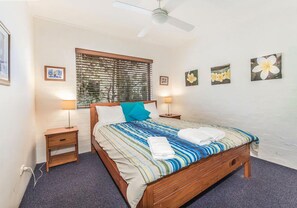 Ein Schlafzimmer mit Bett, einem Fenster mit Jalousien, einem Deckenventilator und Wandlampen.