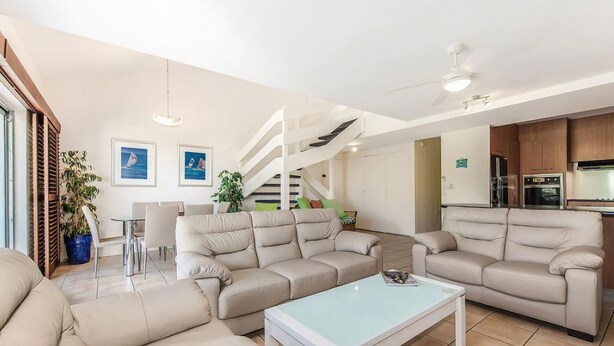 Ein modernes Wohnzimmer mit einer Sofagarnitur, einem Couchtisch und einem Essbereich mit Stühlen. Eine Treppe führt zu einer oberen Ebene.