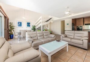 Ein modernes Wohnzimmer mit einer Sofagarnitur, einem Couchtisch und einem Essbereich mit Stühlen. Eine Treppe führt zu einer oberen Ebene.