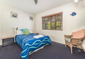 A bedroom with a bed, a chair, a window with blinds, and a ceiling fan.