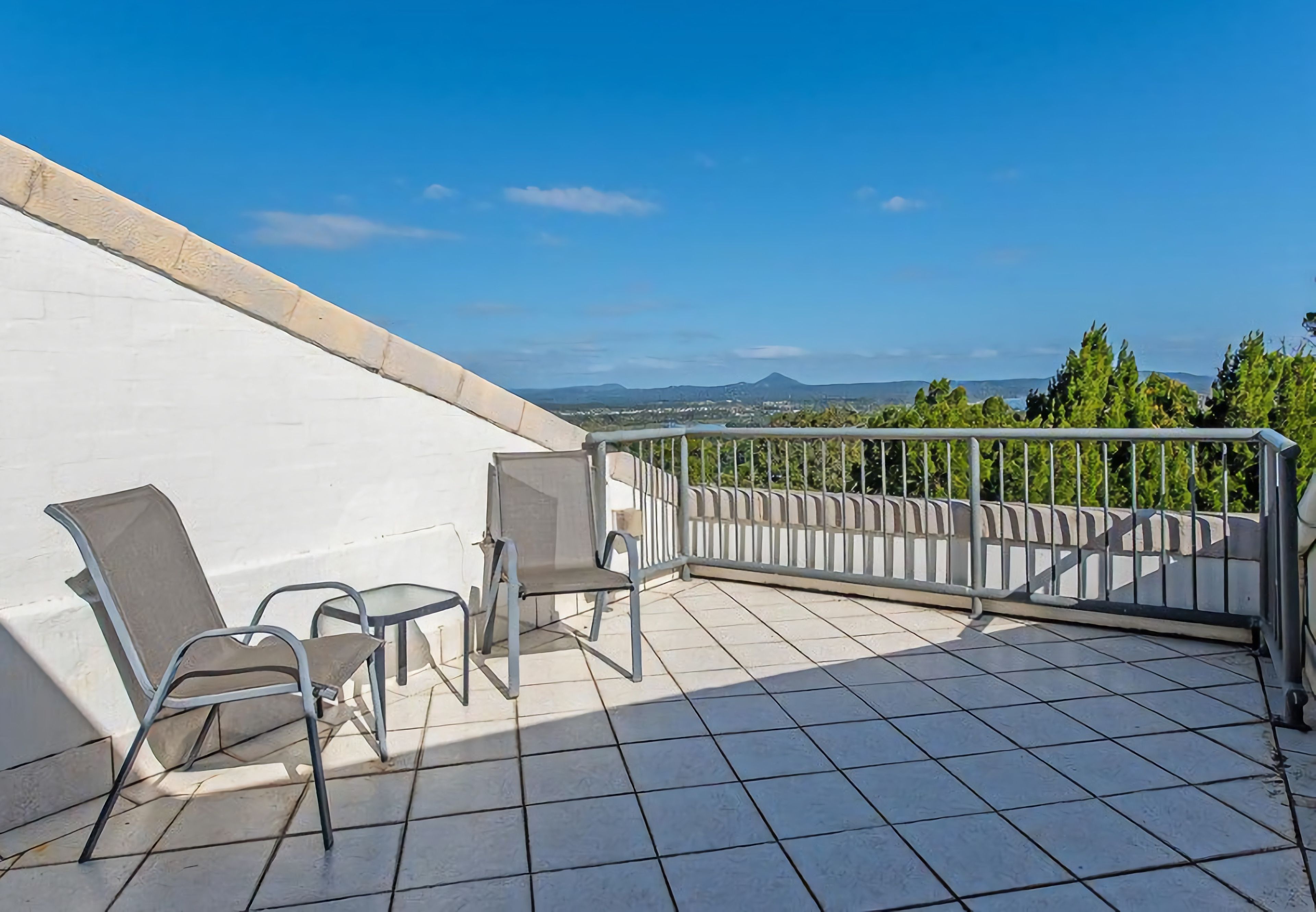 Eine Terrasse mit weißer Wand, Metallgeländer und Blick auf die Landschaft.