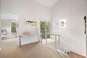 A modern interior with a white console table, a wall-mounted light fixture, and a view through a glass door.