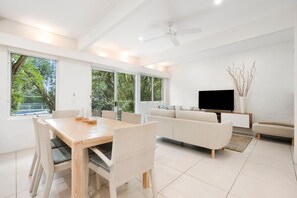 Un soggiorno moderno con zona pranzo, ampie finestre, TV a schermo piatto e ventilatore a soffitto.