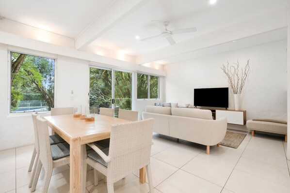 A modern living room with a sofa, TV, and dining area with chairs and a table.