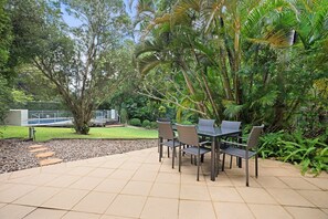 An outdoor patio with a table and chairs, surrounded by lush greenery and trees.
