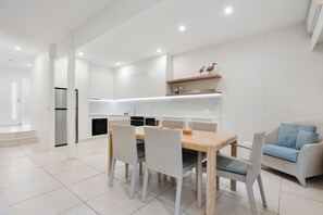Una cucina moderna con mobili bianchi, una zona pranzo con sedie in vimini e un divano con cuscini decorati.