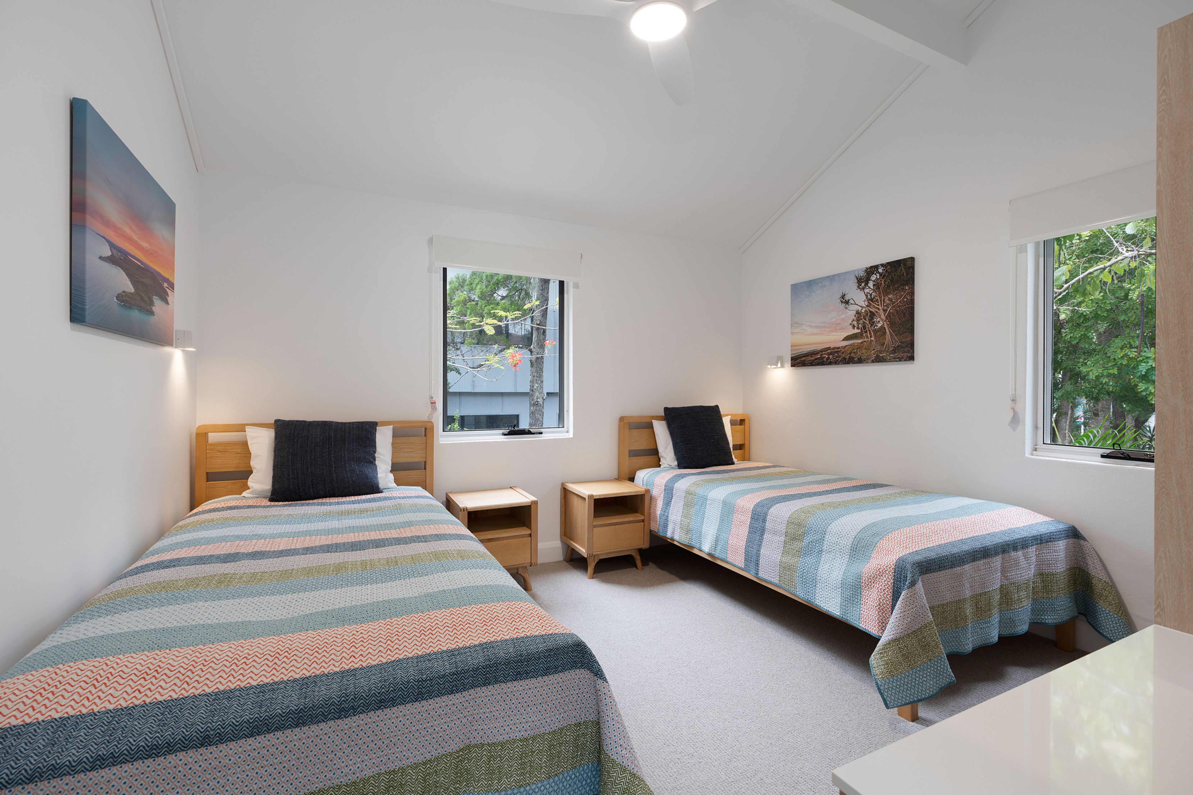 A bedroom with two single beds, a window, and artwork on the walls.