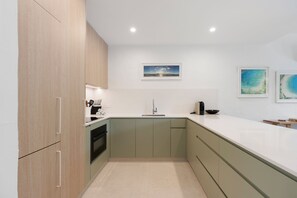 A modern kitchen with light wood cabinets, a white countertop, and a sink. There are two framed artworks on the wall.