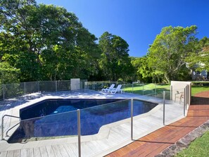 Una piscina con un pontile in legno e poltrone da sdraio bianche.