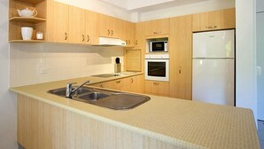 A modern kitchen with wooden cabinets, a built-in microwave, oven, and a stainless steel sink.