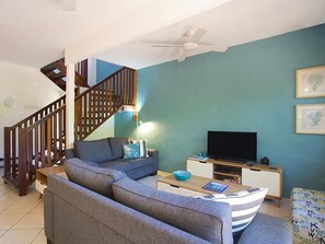 Un soggiorno con divano, televisore, una scala in legno e una ventola a soffitto.