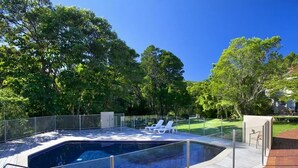 A rectangular swimming pool with a glass edge, surrounded by a wooden deck and metal railing.