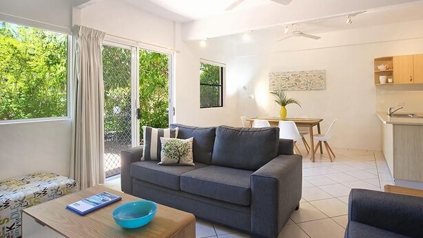 A modern living room with a grey sofa, a wooden coffee table, and a dining area with a table and chairs.