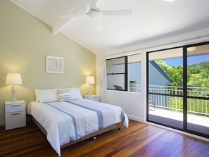 Una camera da letto con un letto, comodini, lampade, una ventola a soffitto e un'ampia porta scorrevole in vetro che dà su un balcone esterno.