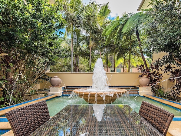Un patio con una fuente central, rodeado de exuberante vegetación y una piscina.
