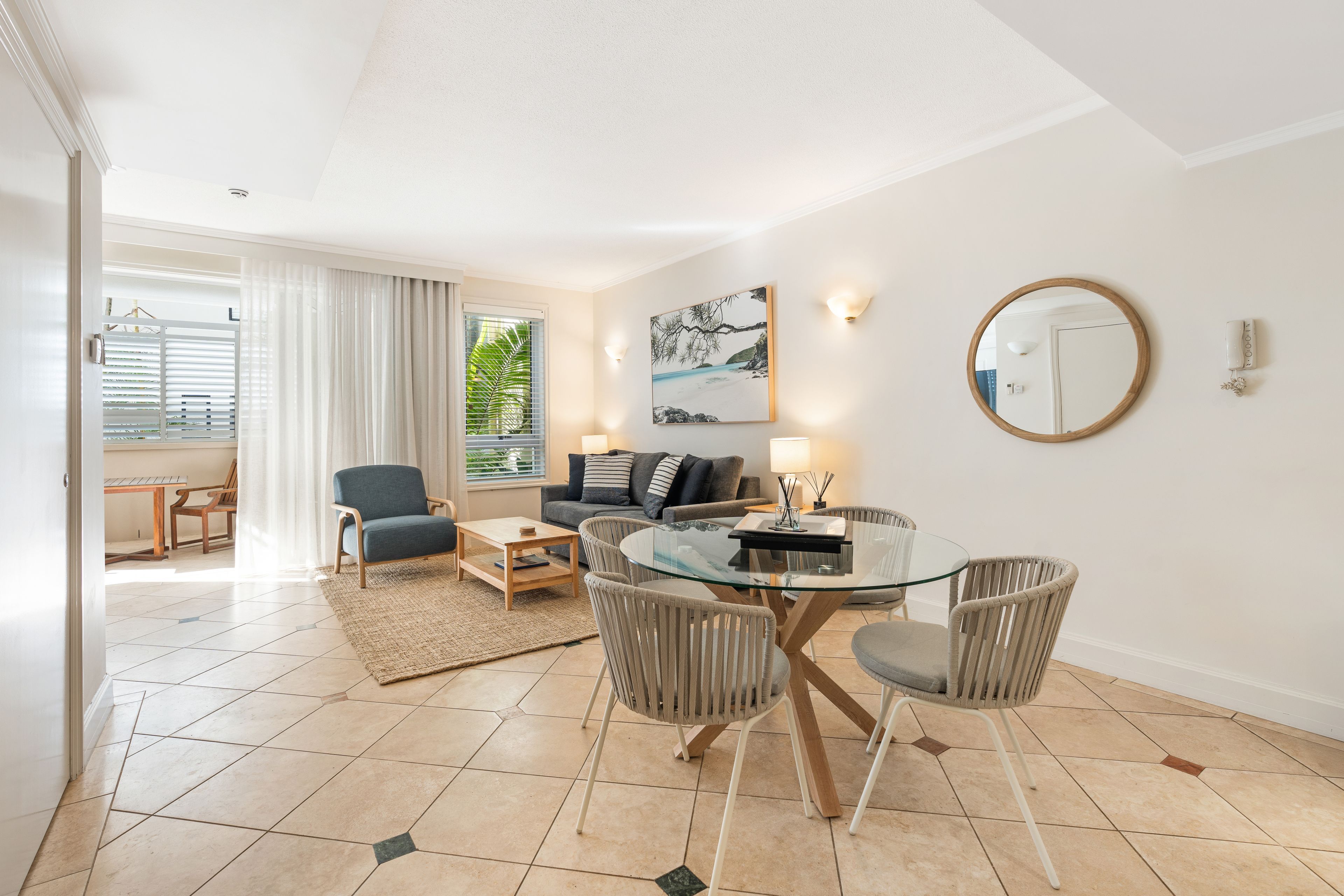 A modern living room with a glass-top dining table, comfortable seating, and a view of the outdoors.