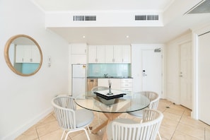 Une cuisine moderne avec des meubles blancs, une table à manger en verre et des chaises en osier.
