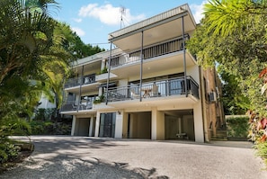 Un edificio a più piani con balconi, un ingresso coperto e una strada di accesso staccionata.