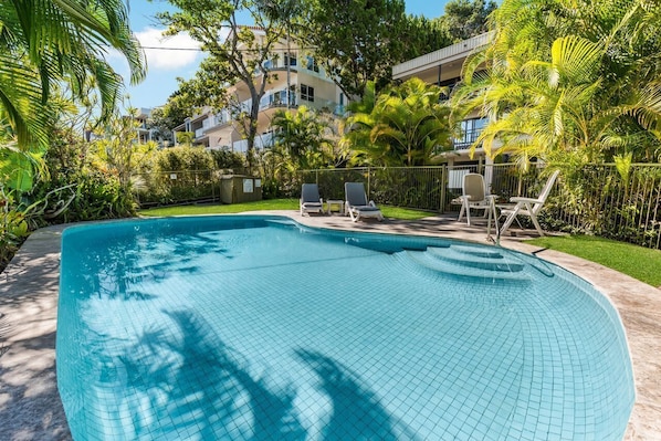 Piscina con bordi piastrellati, immersa nel verde e recintata.
