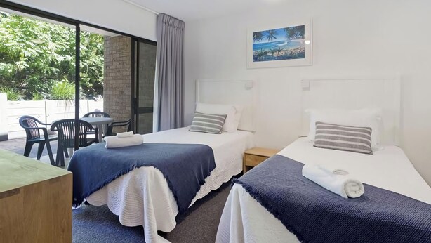 Ett hotellrum med två sängar, ett skrivbord och utsikt över grönområden utanför.