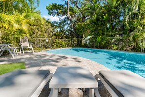 Piscina com espreguiçadeiras e gramado, rodeada por vegetação exuberante.