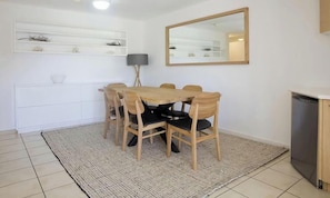 A dining area with a wooden table and chairs, a white cabinet, a mirror, and a floor lamp.