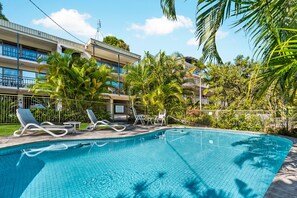 A swimming pool with lounge chairs and palm trees, surrounded by a building with balconies. - Sundown Lodge 1 Edgar Bennett Avenue 14 (Noosa Heads)