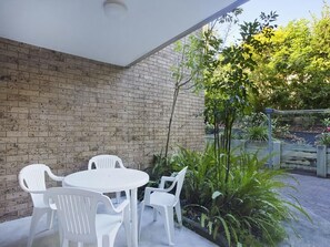 A patio area with a brick wall, white plastic chairs, and a round table.