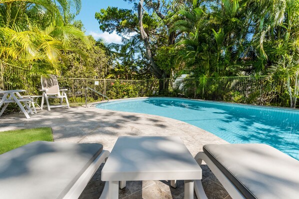A swimming pool with lounge chairs and a grassy area, surrounded by lush greenery.