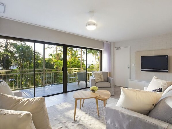 A modern living room with a balcony, a flat-screen TV, and a sofa.