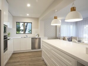 Una cucina moderna con mobili bianchi, lavastoviglie in acciaio inox e una grande isola con cassetti.