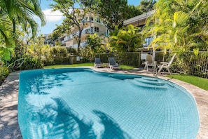 A swimming pool with tiled flooring, surrounded by greenery and a fence.