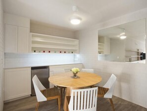A modern kitchen with white cabinetry, a wooden dining table, and white chairs.