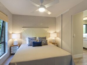 A bedroom with a bed, two bedside tables with lamps, a ceiling fan, and a brick-patterned wall.