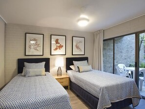 Une chambre d’hôtel avec deux lits, une table de chevet, une lampe et des œuvres d’art encadrées accrochées au mur.