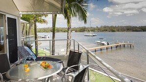 Un balcon avec une table dressée pour deux personnes, donnant sur une étendue d’eau calme où flottent des bateaux.