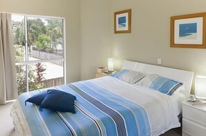 Une chambre avec un grand lit, deux tables de chevet, une fenêtre donnant sur un paysage verdoyant et deux tableaux encadrés accrochés au mur.