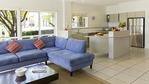 Un salon moderne avec un canapé bleu, une table basse et un coin cuisine comprenant un réfrigérateur et une table à manger.