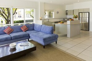 Una sala de estar moderna con un sofá azul, una mesa de centro y una zona de cocina con un refrigerador y una mesa de comedor.