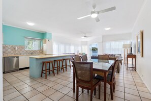 Una cucina moderna con isola centrale, zona pranzo con sedie in vimini e vista mare.