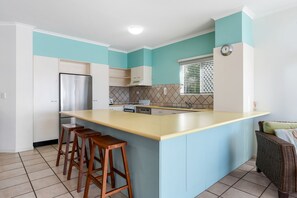 A kitchen with a central island, bar stools, a refrigerator, and a window with blinds.