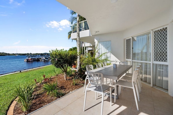 A modern outdoor dining area with a view of the water, a pool, and a boat dock.