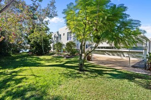 Un giardino curato con diverse piante e arbusti, un viale lastricato e un edificio con un cartello che riporta la scritta 'NOSA RIVER GARDEN'.