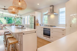 A modern kitchen with white cabinetry, a central island with stools, a stove, and a large window with blinds.