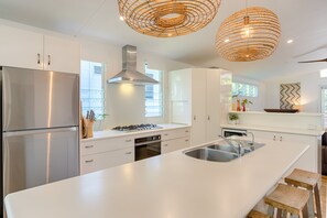 A modern kitchen with white cabinetry, stainless steel appliances, a large island with a sink, and two wicker pendant lights. - Sunshine Beach House - Beautiful parts of nature (Sunshine Beach)
