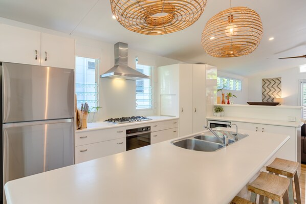 A modern kitchen with white cabinetry, stainless steel appliances, a large island with a sink, and two wicker pendant lights.