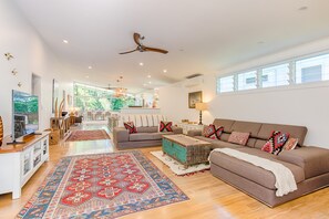 A spacious living area with a large sofa, a coffee table, and a TV. There is a patterned rug on the floor and a ceiling fan.